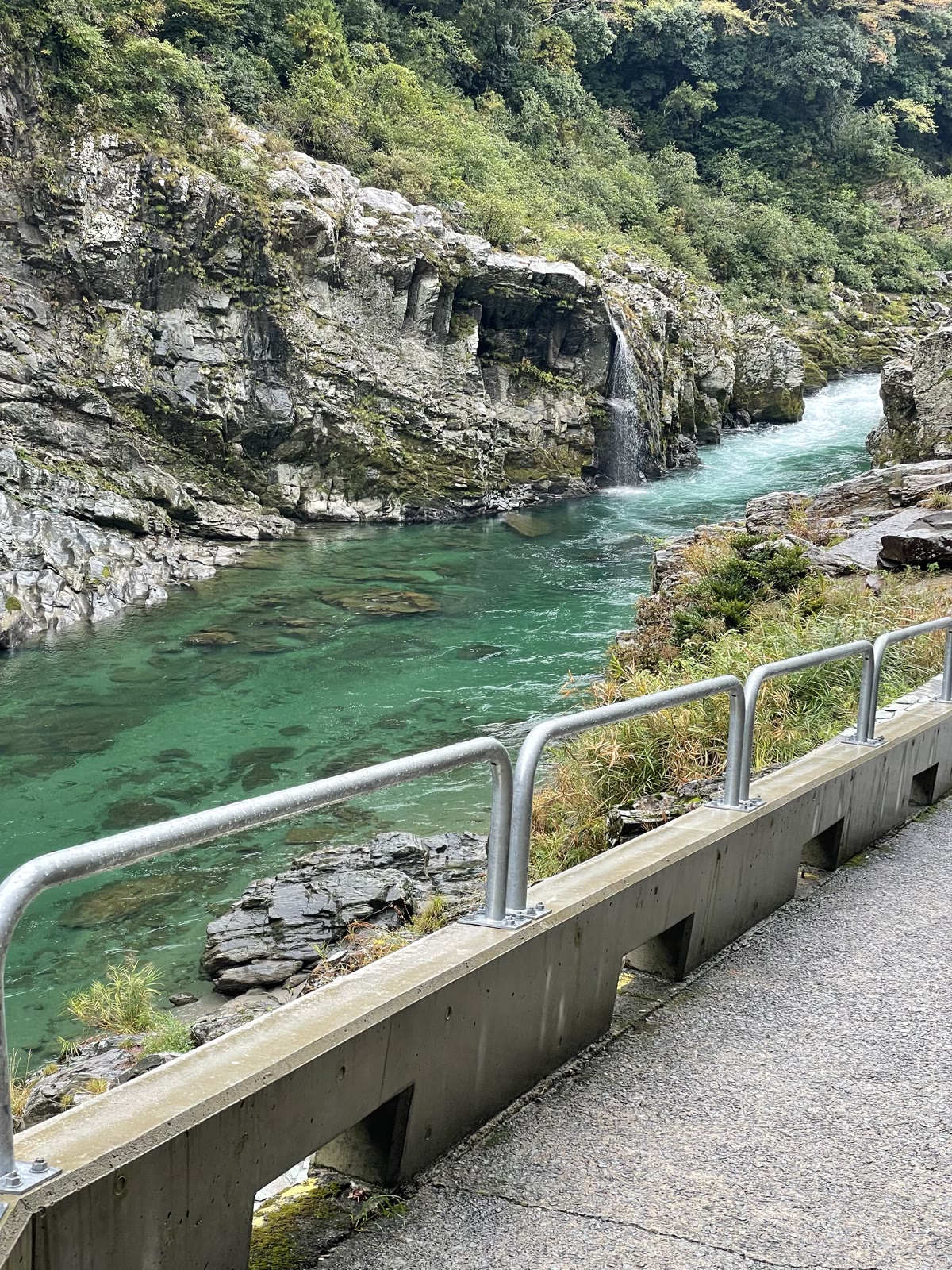 エメラルドグリーンの川と岩壁、小さな滝
